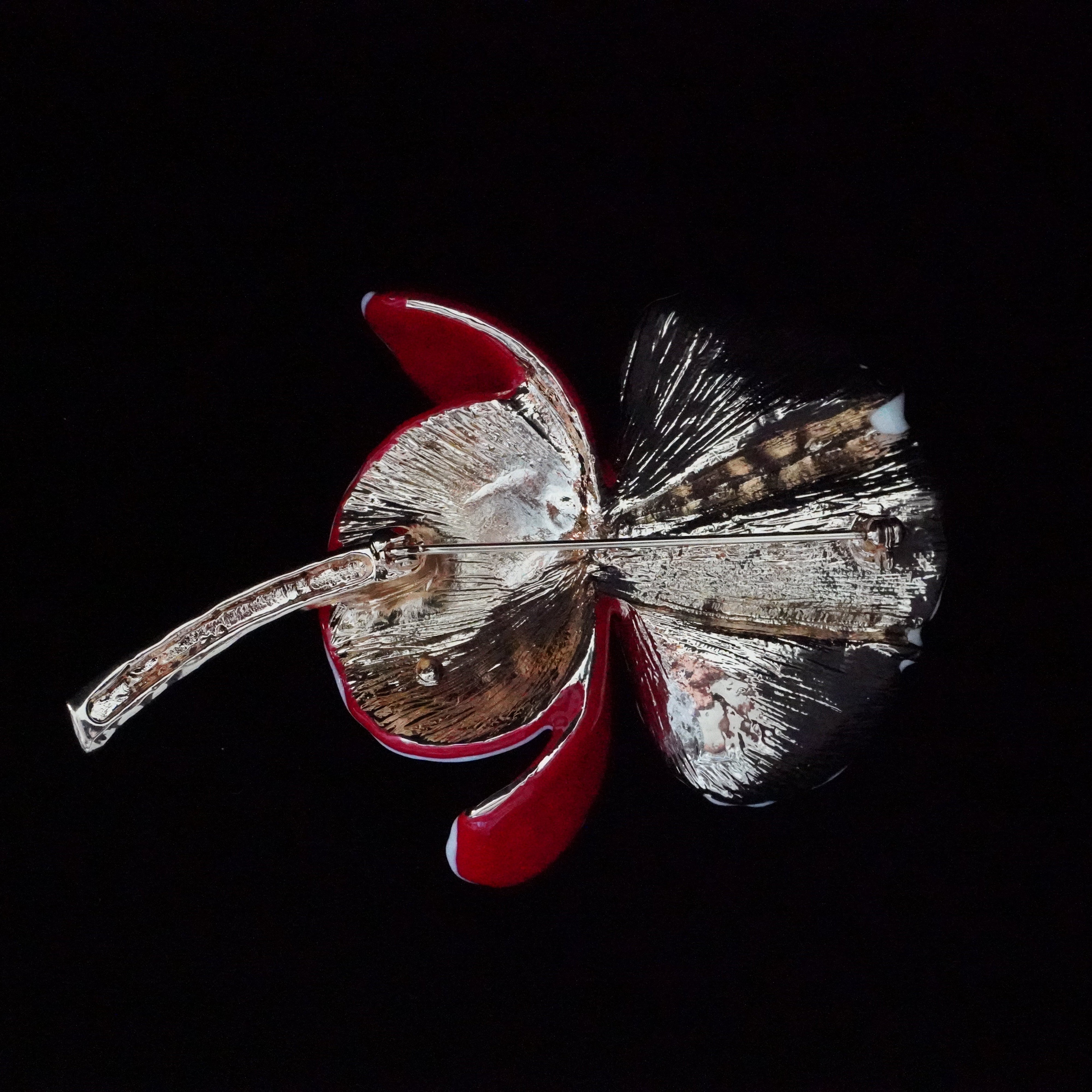 Decorative brooch with red and silver design on a black background