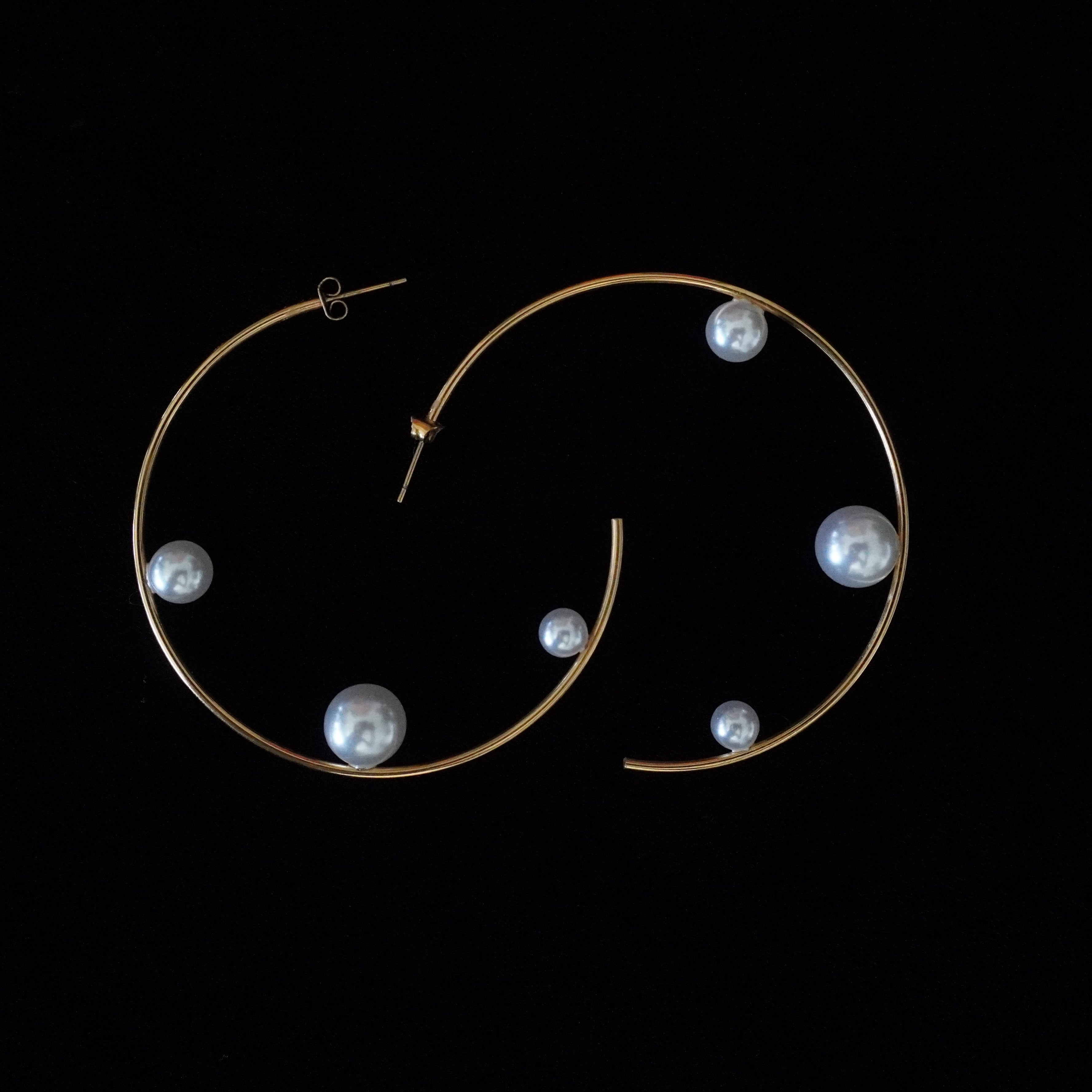 Gold hoop earrings with irregular white pearl-like beads, displayed against a solid black background.